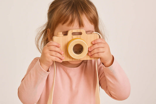 Bambina che gioca con una macchina fotografica in legno ispirata ai giochi in legno Montessori.