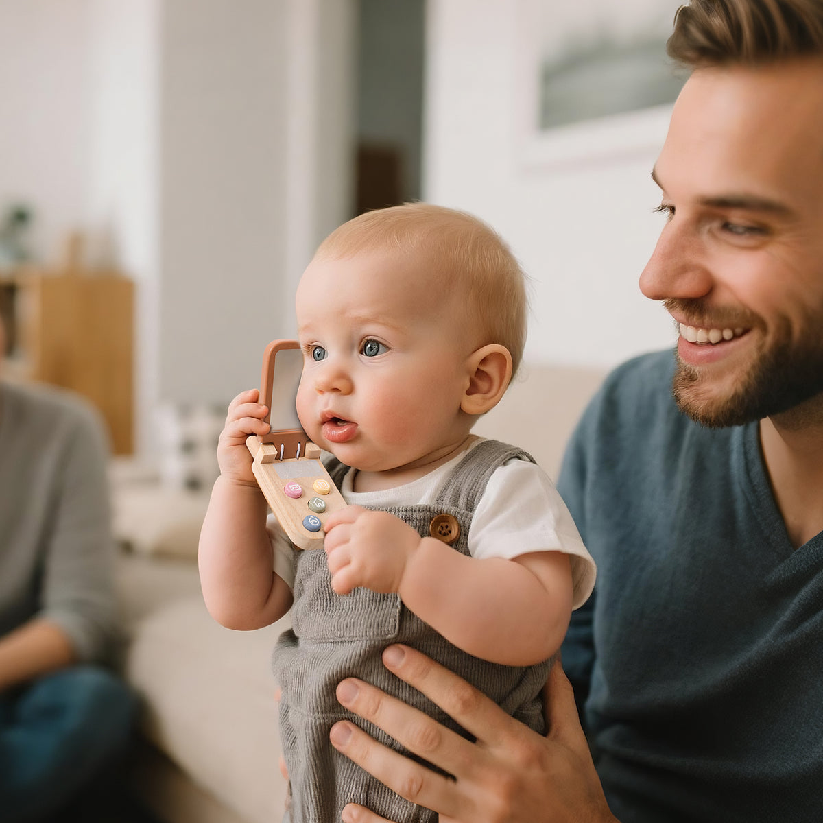 Un papà tiene il bambino che gioca con un telefono in legno, uno dei giochi in legno perfetti per stimolare il linguaggio.